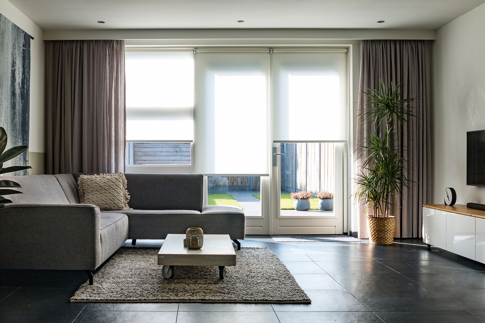 Un salon contemporain avec un canapé gris et une grande baie vitrée donnant sur un jardin
